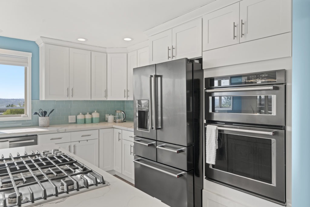White modern kitchen interior with a black fridge next to double ovens surrounded by white shaker cabinets.