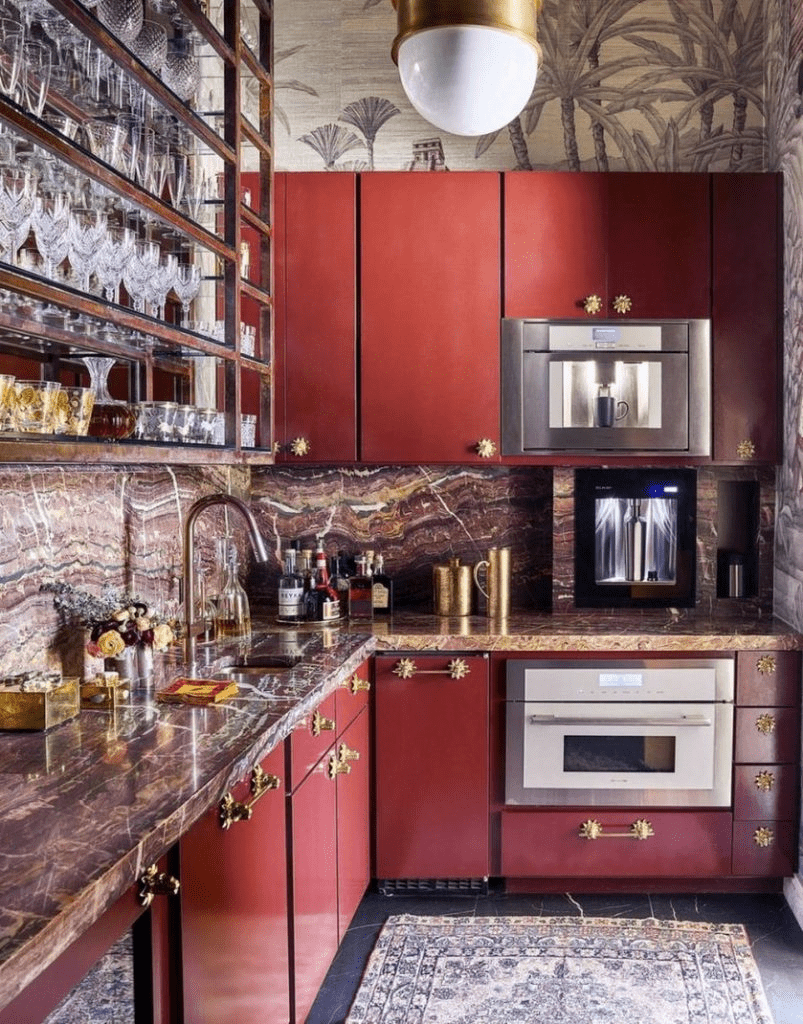 Moody maximalist kitchen with burgundy cabinets, brass cabinet hardware, granite backsplash and countertops, and more.
